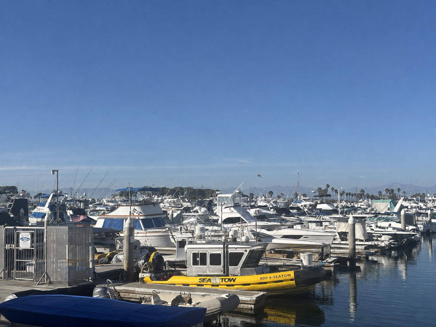 Boats and docks in Huntington Harbour under a clear blue sky, with distant mountains beyond the marina
