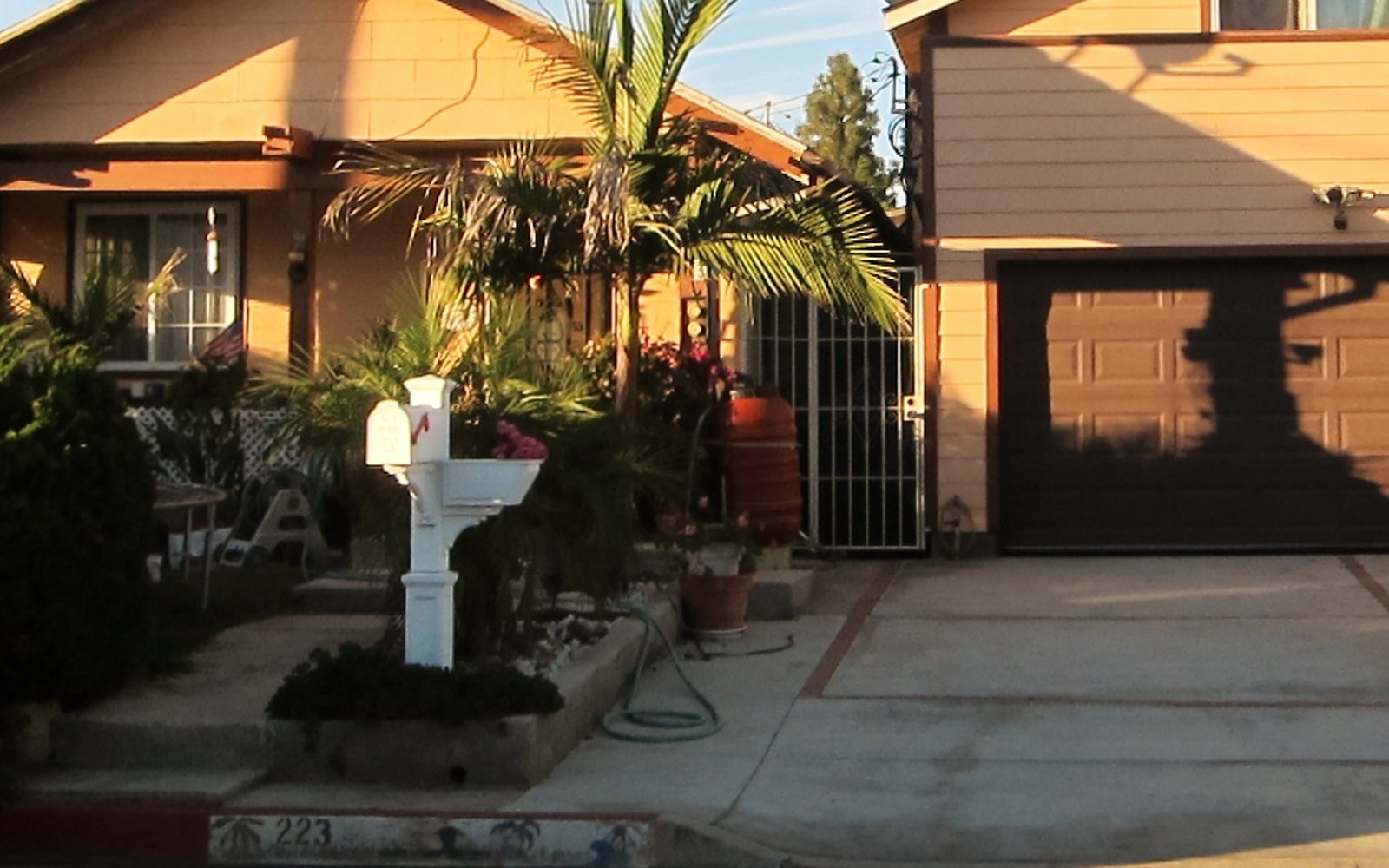 An older single-story Huntington Beach house with mature palms and a white mailbox, standing beside a taller remodeled two-story home next door
