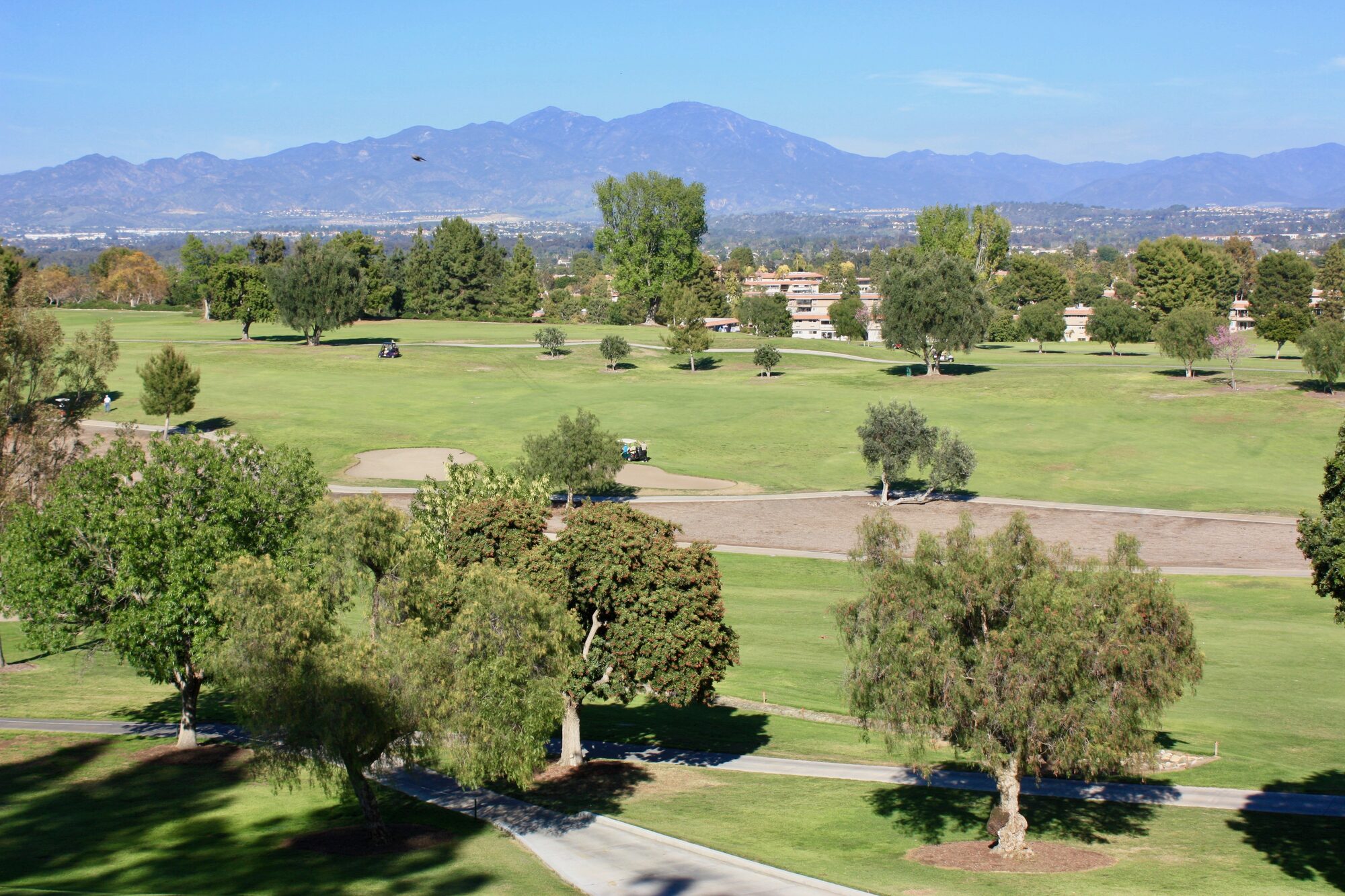 Open green fairways, mature trees and low-rise residences at Laguna Woods Village, with the Saddleback mountains in the distance