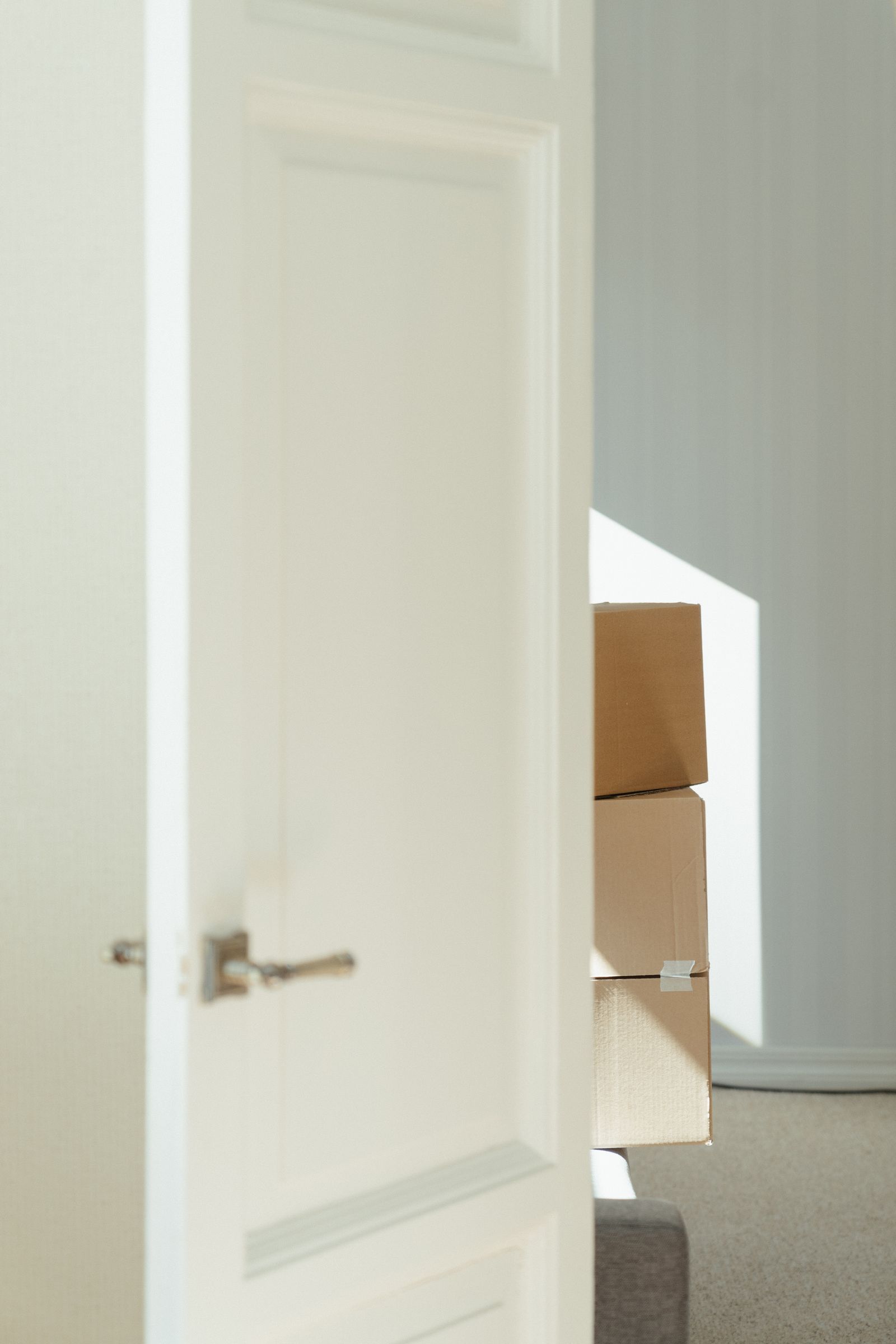 Open white door beside stacked cardboard moving boxes in a bright, sunlit room.